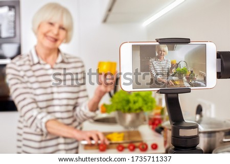 Blurred background isolated on kitchen light interior.Aged female old woman record broadcast live video online cook healthy fitness diet summer food. Lady vlogger blogging has followers youtube chanel