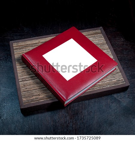 Burgundy photo album with leather binding, picture frame, on a dark table.