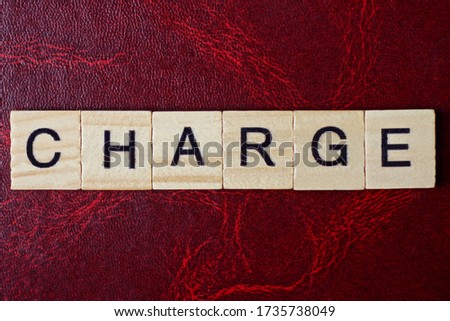 text the word charge from gray wooden small letters with black font on an red table