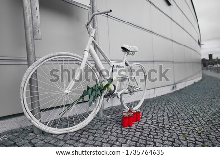 Berlin Germany, white ghost bike as a memorial to a biker who was killed in Berlin city traffic, closed near the city center, white roses with green leaves and red candles as a commemoration