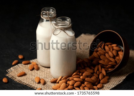lactose-free almond milk in bottles with nuts on a dark black table, vegetarian milk drink, healthy milk product