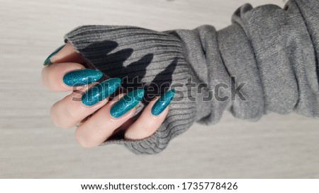 Female hand with long nails and light blue turquoise manicure with bottles of nail polish