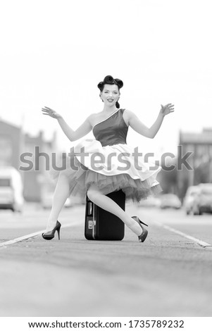Black and white retro style photo. A girl in a dress and hairstyle in the style of the 40-50s on a city street on tram tracks on a sunny day
