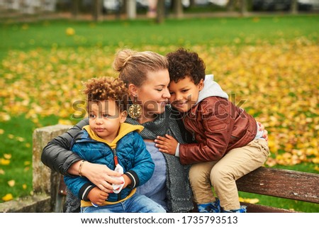 Outdoor portrait of happy young mother with two lovely sons, family enjoying nice autumn day in public park, mixed race family