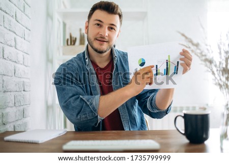 Smiling young businessman sit at desk and talk by webcam with business colleague, shows a graph with the dynamics of economic growth and discusses about further strategy. Distant work Royalty-Free Stock Photo #1735799999