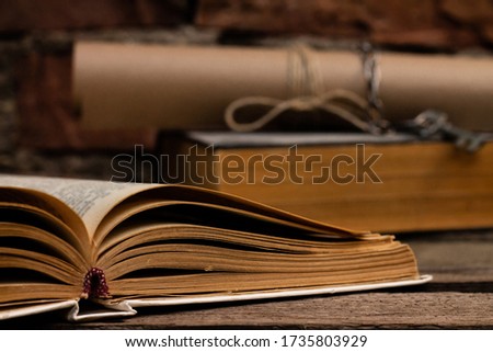 Old books with a scroll and key on a rustic wooden surface on a brick wall background