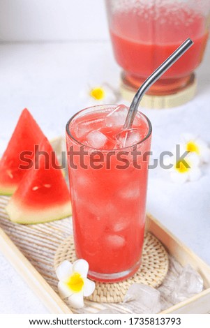 Selective focus of a glass of cold watermelon juice on a white wooden tray.