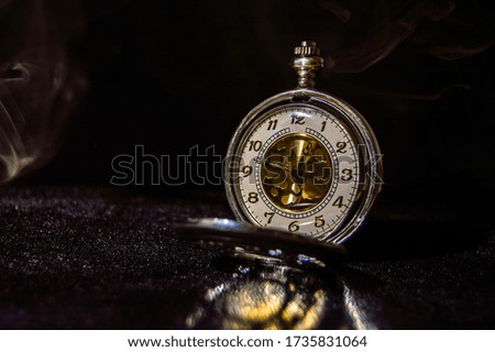 The pocket watch stands on a dark glossy surface
