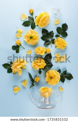 Creative layout made of glass tea pot with yellow roses and leaves on blue background. Top view, Flat lay.