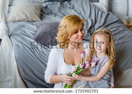 Happy women 's day. Happy mother 's day. A child-daughter congratulates her mother and gives her flowers-tulips. Mom and girl smile and hug. Family holiday and unity.