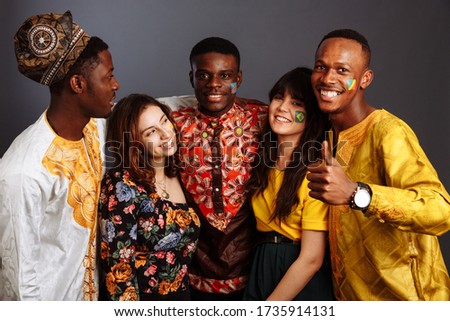Peaceful Concept of friendship and peace between countries: three African men and two Latin ladies in national clothes show thumb up hug together with body arts flags Congo, Nigeria, Brazil, Ecuador