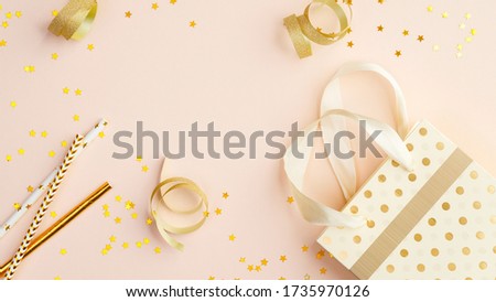 Children birthday party concept. Top view bag with gifts, party serpentine and golden confetti on beige table.