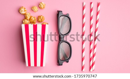 Flat lay composition with popcorn in striped cardboard box, 3d glasses and drink straws on pink background. Watching movie at cinema concept.