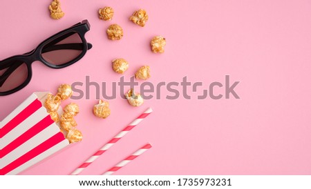 Pop corn in striped red and white cardboard box, 3d glasses, drink straws on pink table top view. Online cinema, watching movie concept.