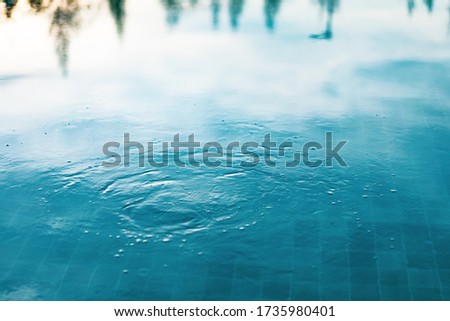 Ripples in the blue swimming pool with a low light of sunset as a background