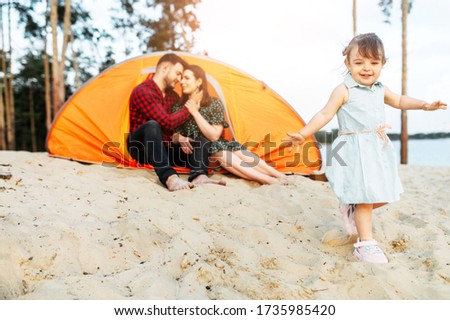 Family time outdoors in a forest. Young parents and cute toddler girl spend active time together, they are living in a camp in a forest
