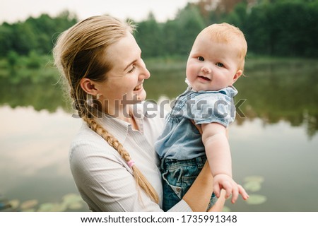 Portrait mom with child together on nature. Mum, little daughter outdoors. Young mother with baby girl walk on beach near lake. Family holiday on pond. Happy Mothers Day. Close up.