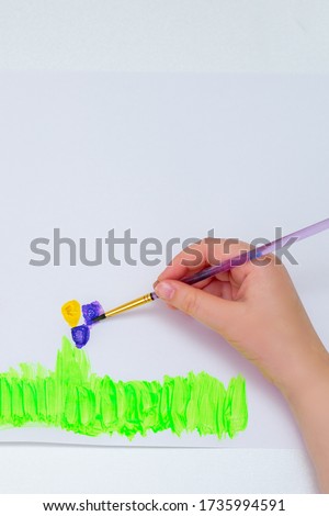 Child's hands drawing flowers on white sheet of paper. Top view. Children's and Earth day concept.
