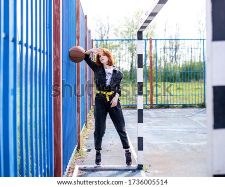 Beautiful red-haired girl with a basketball on the basketball court