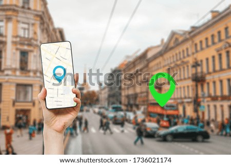 A female's hand holds a smartphone with an online map app. In the background is a city street with traffic, with a green location icon.Concept of online navigation and GPS