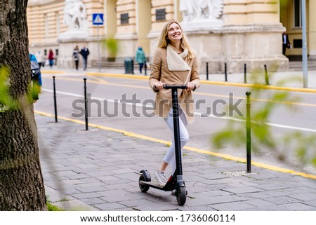 Young blond woman enjoying with electric scooter in city on sidewalk.