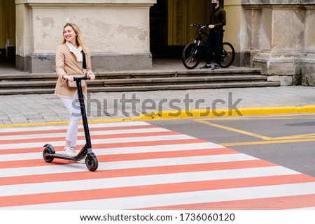 Excited positive emotions female crossing street on pedestrian crossing on an electric scooter. Pedestrian passing a crosswalk. Healthy lifestyle. Eco-friendly transport. Safety concept for road users