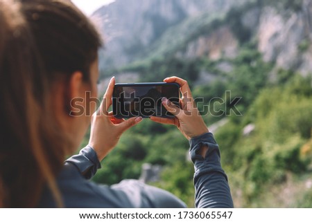 Young female travel blogger making selfie using smartphone on top of mountain on breathtaking scenery, girl wanderlust using telephone for making picture during hiking tour getting to destination.