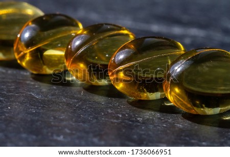 Several capsules of vitamins and minerals, fish oil are stacked in a row against a dark background. Health and Nutrition Supplements