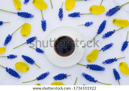 A cup of hot coffee, yellow petals and many small blue spring flowers. The apartment was lying. The concept of holidays and good morning wishes.
