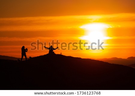 Silhoutte of two happy girls taking pictures and having fun on a top of a moutain in the sunset in Northern Norway