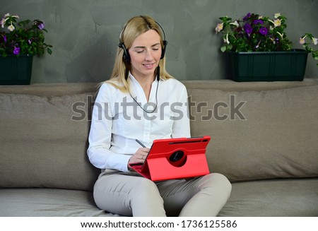 Photo of a pretty business blonde girl talking on a tablet. Caucasian model posing at home sitting on a sofa with a smile.