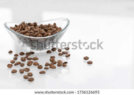 Coffee beans in a glass bowl on a glossy light table. some grains are scattered on the table. breakfast concept
