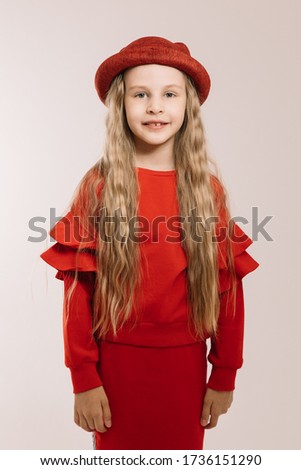 Little girl in a red suit and hat posing on a light background