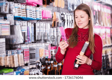 Young woman is choosing modern comb for her hair in the shop
