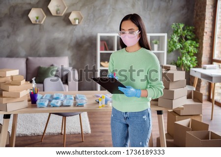 Photo of asian lady business organized orders facial flu medical masks packs for delivering boxes waiting post service hold clipboard checking information numbers home office indoors