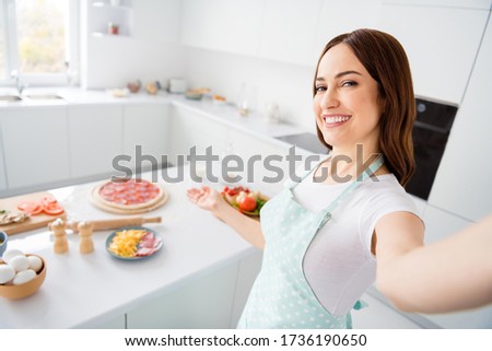 Portrait of positive charming girl cook homemade pizza make selfie demonstrate pastry italian dish wear dotted apron in house indoors kitchen