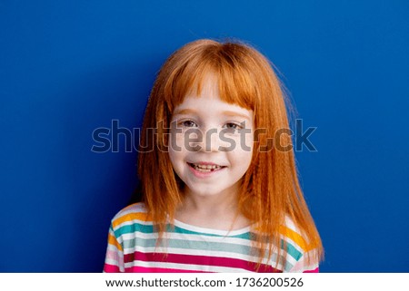 little girl with red hair in a multicolored smile stands on a bl