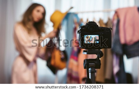 Fashion blogger. Young attractive woman travel vlogger showing a new hat to the camera, getting ready for the trip. The camera on tripod in the foreground recording the vlog. Blog as a lifestyle