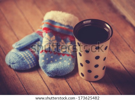 Cup of coffee and mittens on wooden table. Photo in old color image style.