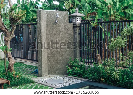 Photo of a summer outdoor shower in the backyard with green grass, trees and a metal fence