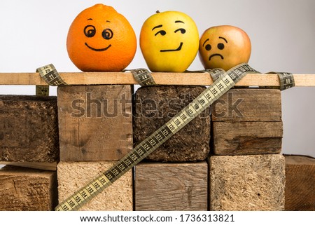 fruit with drawn faces that express different emotions, isolated on a wooden podium with a tape measure