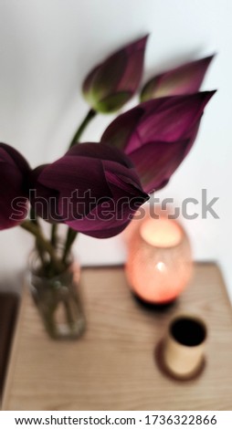 Lilac lotus flowers in a vase on the table. Against the background of coffee in a wooden glass and a bamboo lamp