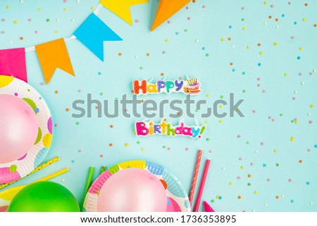 Paper tableware for a holiday. Birthday party decoration on a blue background. Frame or background with colorful plates, a carnival cap and streamers. Eco-friendly food items.