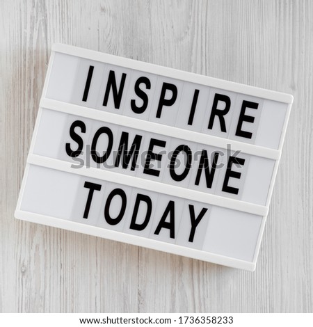 'Inspire someone today' words on a lightbox on a white wooden background, top view. Overhead, from above, flat lay. 