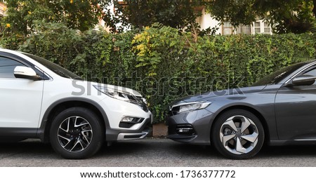 Closeup of front side of white and grey cars  parking in the opposite direction on the road with natural fence  background. Royalty-Free Stock Photo #1736377772