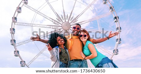 Happy multicultural friends having fun standing at ferris wheel - Cheerful multiracial students embrace in positive attitude posing for the photo - Concept of friendship travel and joy  - Image