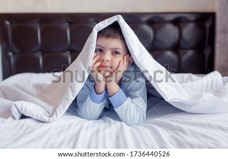 
A young brunette boy is lying in bed. Blanket on the head