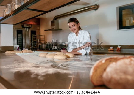 Young female baker preparing dough for bread in modern manufacturing.