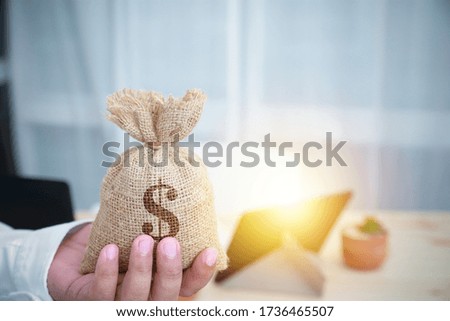 Close-up hand businessman holding a sack of money dollar in hand his with tablet and the desk in an office copy space for write text, background. Concept business, financial, and banking.
