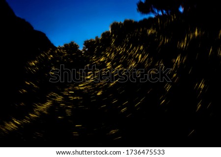 Vibrant yellow circling light streaks on silhouetted mountainside landscape on vibrant blue early night sky - abstract rotational motion blurred background, texture 